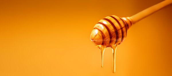 عسل می ریزد از چکه های عسلی چوبی بر روی زمینه زرد محصول زنبور عسل شیرین برای طراحی شما با copyspace