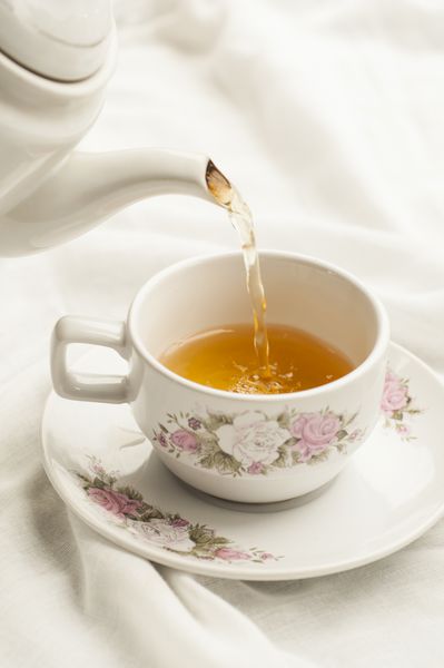چای ریخته شده در فنجان چای در زمینه پارچه سفید