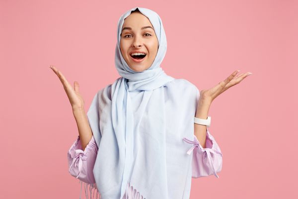 مبارک شگفت زده زن عرب در حجاب پرتره دختر خندان قرار گرفتن در پس زمینه استودیوی صورتی زن عاطفی جوان احساسات انسانی مفهوم بیان صورت نمای جلویی