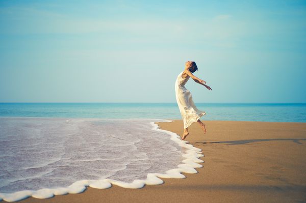 خانم جوان با لباس سفید که در ساحل می پرید