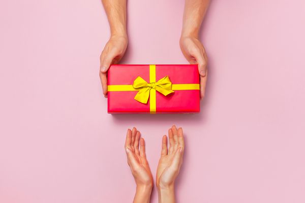 نمای بالای دستان زن و مرد که دارای جعبه هدیه قرمز با روبان طلایی در زمینه صورتی هستند تخت خواب هدیه برای تولد روز کریسمس سال نو تبریک فضای کپی پس زمینه