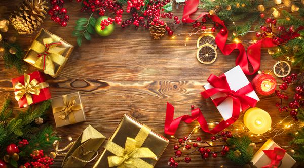 زمینه هدایای کریسمس قاب بک گراند زیبا و سال نو با جعبه هدیه های پیچیده رنگی کباب ها شمع ها و گلدان های روشنایی بر روی زمینه میز چوبی با درخت صنوبر نمای بالا