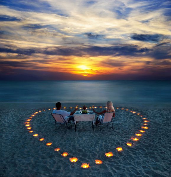 یک زوج جوان یک شام عاشقانه با قلب شمع در ساحل شن دریا به اشتراک می گذارند