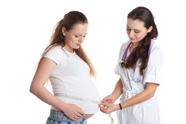 پزشک زن شکم زن باردار را با زمینه سفید اندازه گیری می کند