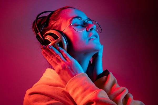 زن زیبا مد با هدفون گوش دادن به موسیقی در پس زمینه نئون قرمز در استودیو