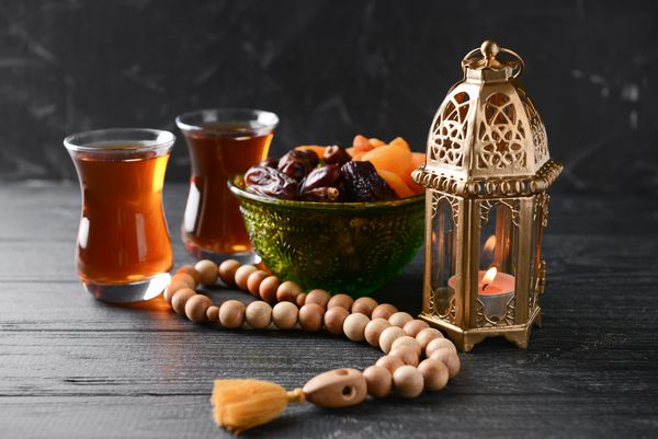 لامپ مسلمان میوه های خشک چای و طعبی روی میز چوبی