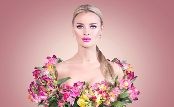 دختر مدل زیبایی در لباس تابستانی که از گلهای رنگارنگ تازه ساخته شده است زیبا و عاشقانه زن جوان رمان بهار با گل دسته گل Alstroemeria با زمینه رنگ صورتی آرایش کامل