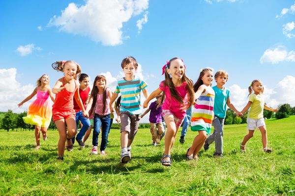 بسیاری از بچه ها پسران و دختران مختلف در روز تابستان آفتابی با لباس های گاه به گاه در پارک در حال دویدن هستند