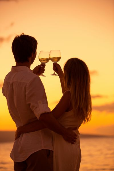 شبح زن و شوهر که از غرق لیوان شامپاین در ساحل گرمسیری هنگام غروب خورشید لذت می برند