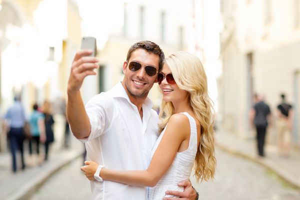 تعطیلات تابستانی فناوری عشق رابطه و دوستیابی زن و شوهر لبخند که با تلفن هوشمند در شهر سلفی می گیرند