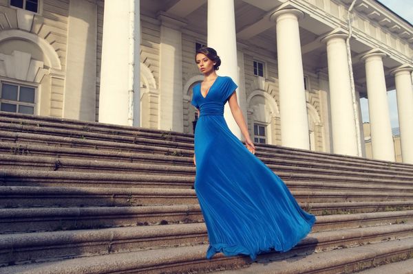 پرتره سبک زن ظریف جوان با لباس بلند پرواز آبی که در پله ها در برابر ساختمان شهر قدیمی قرار گرفته است