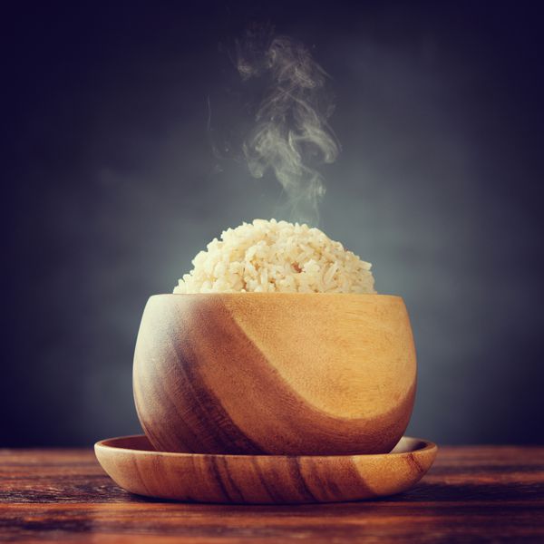 برنج قهوه ای باسماتی ارگانیک طبخ شده در کاسه چوبی با دود بخار روی میز ناهار خوری تنظیم نور کم با سبک احیا یکپارچهسازی با سیستمعامل