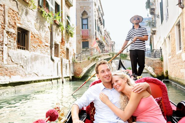 زن و شوهر سفر عاشقانه در ونیز در گوندول سوار عاشقانه در قایق با هم در تعطیلات تعطیلات سفر زن و شوهر زیبا رمانتیک جوان که در کانال گیاهخوار در گوندولا قایقرانی می کنند ایتالیا اروپا