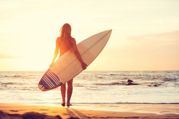 دختر سورپرای زیبا در ساحل هنگام غروب آفتاب