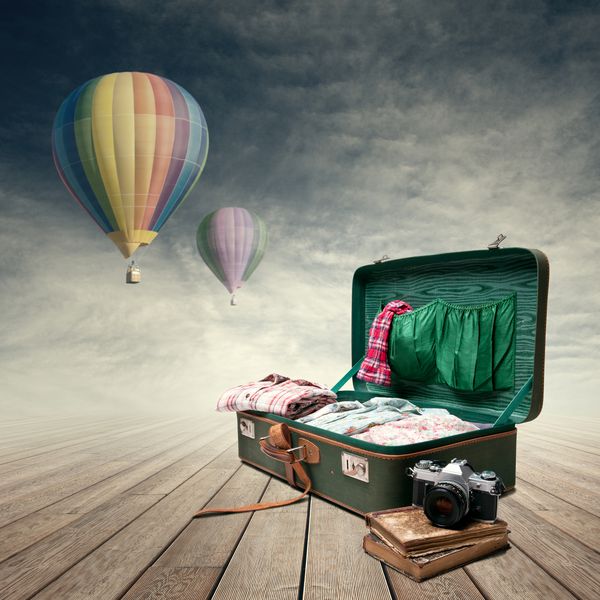 چمدان پرنعمت با کتاب و دوربین قدیمی بالن های هوایی که بر روی پس زمینه پرواز می کنند
