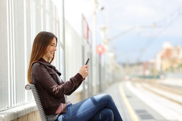 زن در تلفن همراه در ایستگاه قطار با راه آهن در پس زمینه ارسال پیامک