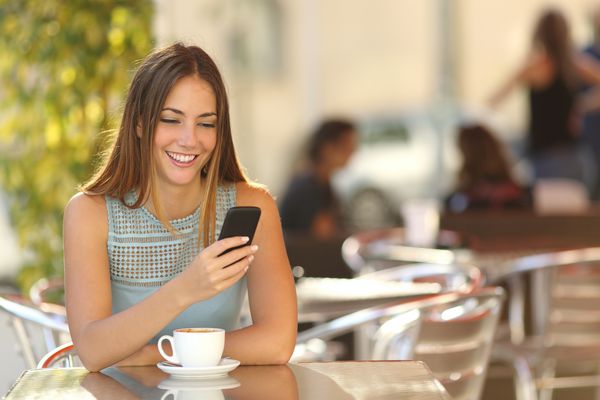 پیام کوتاه دختران با تلفن هوشمند در یک تراس رستوران با پس زمینه تمرکز نشده