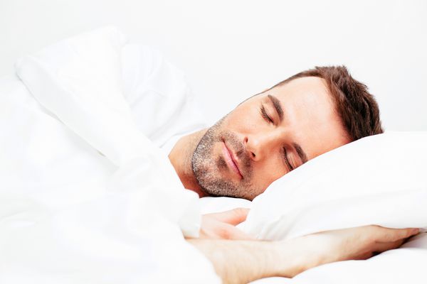 مرد جوان خوش تیپ که در رختخواب سفید خوابیده است