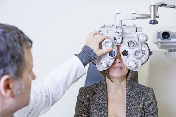 اپتومتریست مرد در حال کالیبره کردن فوروپتر نوری برای معاینه بینایی به تمرکز یک خانم جوان است که در مرکز فوروپتر تمرکز دارد