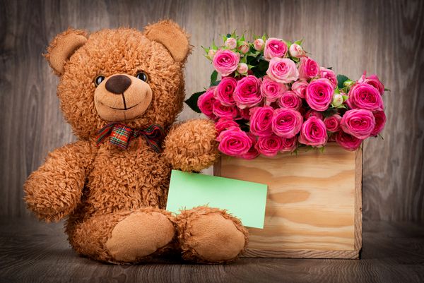 گل رز در جعبه و یک خرس عروسکی در زمینه چوبی