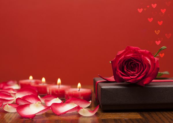 گل سرخ روی جعبه شکلات با شمع و گلبرگهای گل قلبهای رمانتیک در کنار هم قرار گرفت
