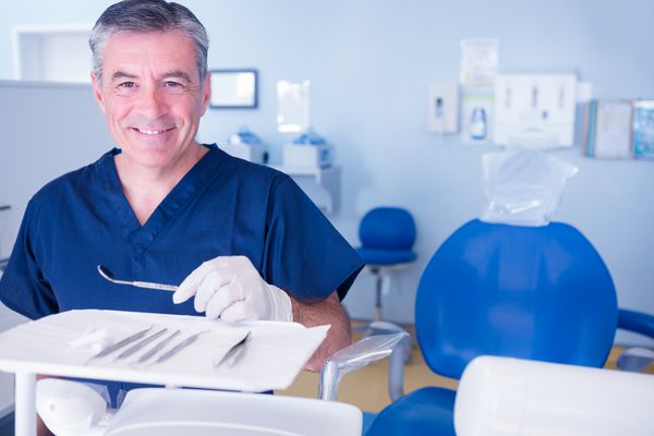 دندانپزشک در اسکراب های آبی که در ابزارهای نگهدارنده دوربین در کلینیک دندانپزشکی لبخند می زنند
