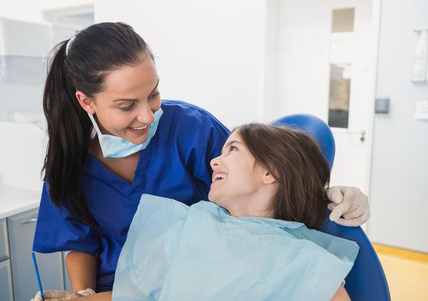 دندانپزشک شاد کودک با داشتن یک بیمار جوان خندان در کلینیک دندانپزشکی