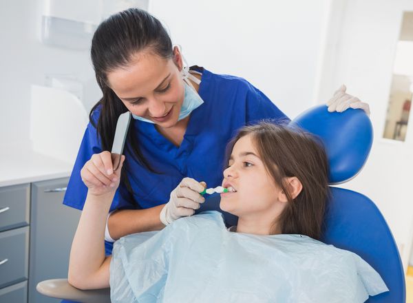 دندانپزشک کودکان در کلینیک دندانپزشکی دندانهای بیمار خود را مسواک می زند