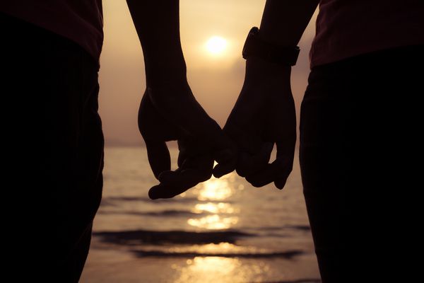 زن و شوهر عاشق انگشتان دست در هنگام غروب خورشید در ساحل روز