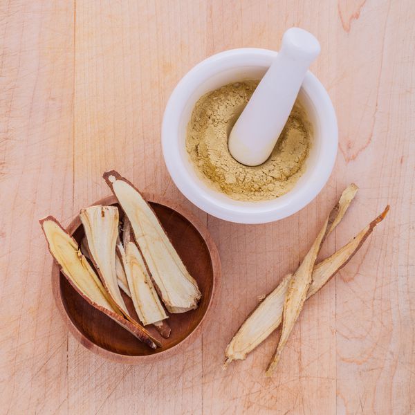 داروهای گیاهی شیرین بیان شامل پودر ریشه خرد شده و خرد شده و ملات روی میز چوبی