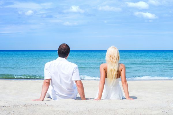زن و شوهر دوست داشتنی که در یک ساحل گرمسیری تابستانی نشسته و در آغوش گرفته اند
