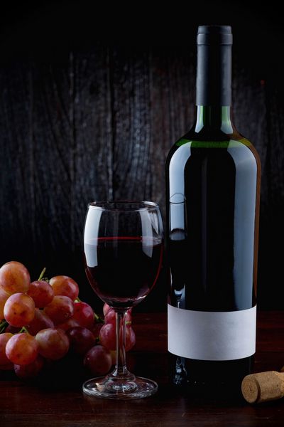 میز شیشه ای با بطری قرمز و خوشه انگور روی میز چوبی