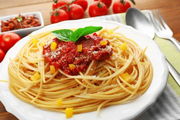 اسپاگتی با سس گوجه فرنگی پاپریکا و پنیر روی بشقاب سفید روی زمینه چوبی رنگی