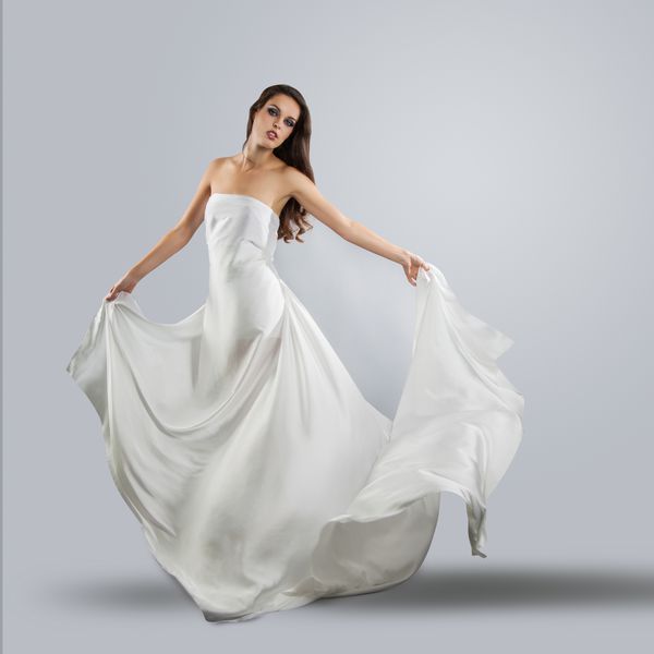 دختر جوان زیبا در لباس سفید پرواز پارچه در حال جریان