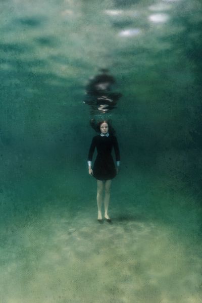زن جوان با لباس مشکی که روی ماسه های زیر آب ایستاده است