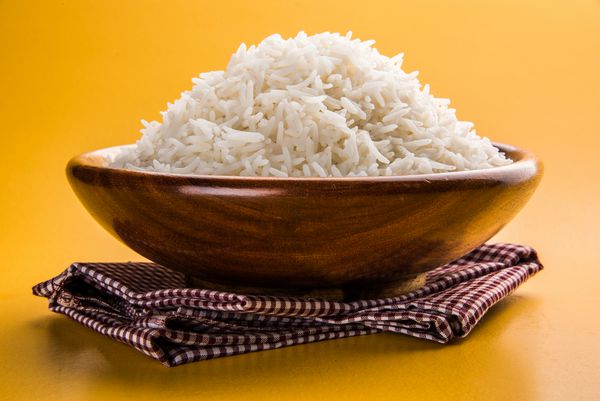 برنج باسماتی ساده پخته شده پخته شده در یک کاسه چوبی جدا شده بر روی زمینه های رنگارنگ یا چوبی
