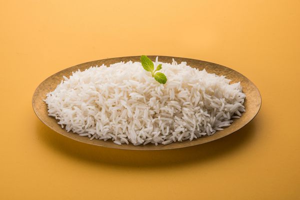 برنج سفید باسماتی ساده پخته شده که در یک کاسه برنجی یا بشقاب سرو شده جدا شده بر روی زمینه رنگی یا چوبی
