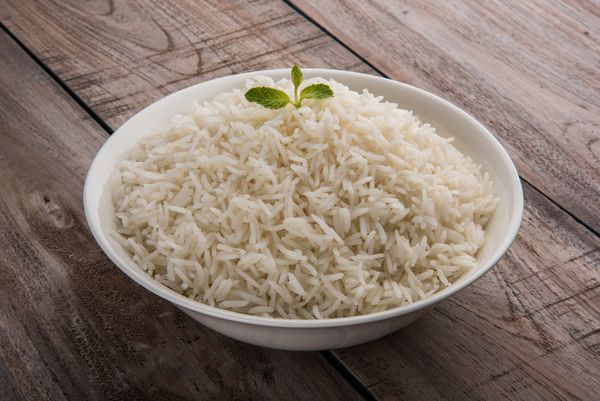 برنج سفید باسماتی ساده پخته شده که در یک ظرف یا بشقاب سرامیکی سرو می شود که بر روی زمینه رنگی یا چوبی جدا شده است