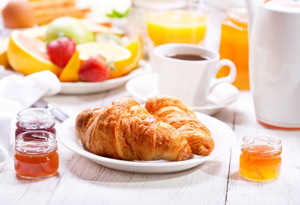 میز صبحانه با کروسان قهوه آب پرتقال نان تست و میوه