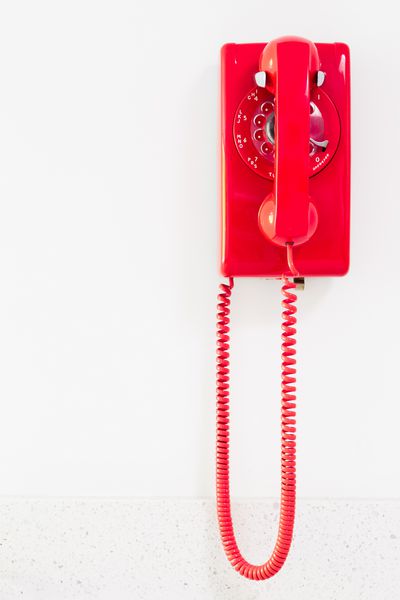 تلفن قرمز پرنعمت آویزان بر روی دیوار سفید