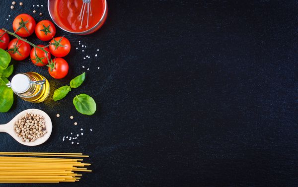 مواد ماکارونی گوجه فرنگی روغن زیتون سیر گیاهان ایتالیایی ریحان تازه نمک و اسپاگتی در زمینه سنگ سیاه با فضای کپی افقی نمای بالا