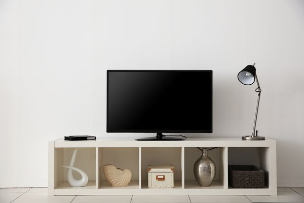 تلویزیون صفحه گسترده روی ایستاده سفید در نزدیکی دیوار نور