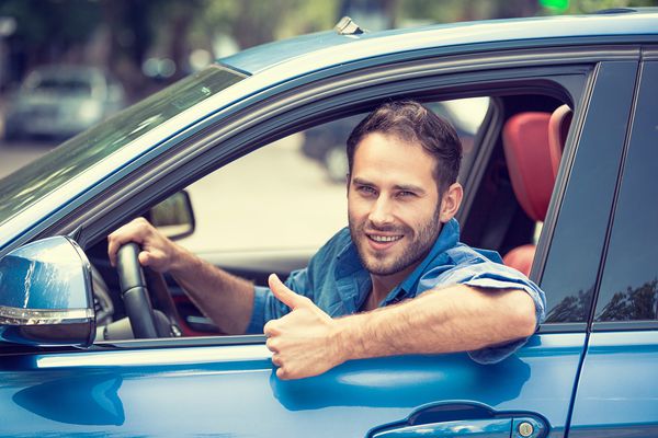 پنجره کنار ماشین راننده مرد لبخند نشان دادن شستن رانندگی اتومبیل ورزشی آبی جدا شده در پس زمینه پارکینگ مرد جوان خوش تیپ از وسیله نقلیه جدید خود هیجان زده است بیان صورت مثبت