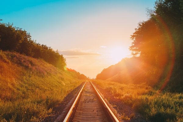 منظره زیبا با راه آهن پیش رو مستقیم از طریق مزارع تابستانی تابستانی تا غروب خورشید یا طلوع آفتاب در آفتاب اثر شعله ور شدن لنز