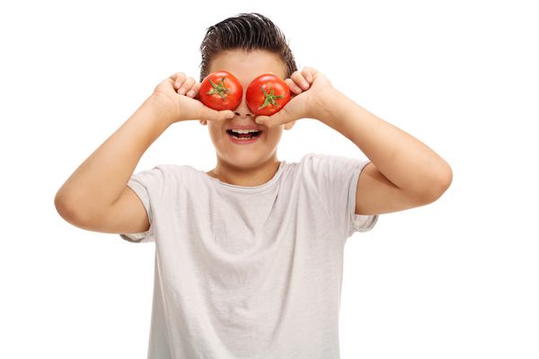 بچه بازیگوش که دو گوجه فرنگی روی چشمش نگه داشته و لبخند بریده شده در زمینه سفید دارد