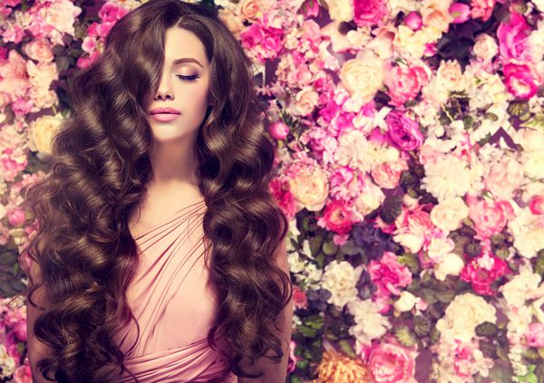 دختر با موهای بلند و براق زن حالت زیبا با مدل موهای مجعد دیوار پس زمینه گل