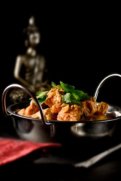 مرغ پیچ خورده هندی کلاسیک با گشنیز گوجه فرنگی و عسل با یک سس نارگیل ماریناد غنی که در برابر پس زمینه تیره هندی قرار دارد فضا را کپی کنید