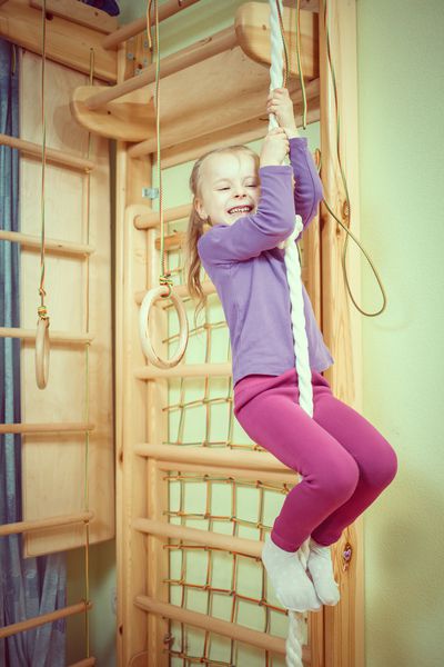 دختر زیبا ورزشکار در اتاق کودکان و نوجوانان در میله های دیواری ورزش می کند
