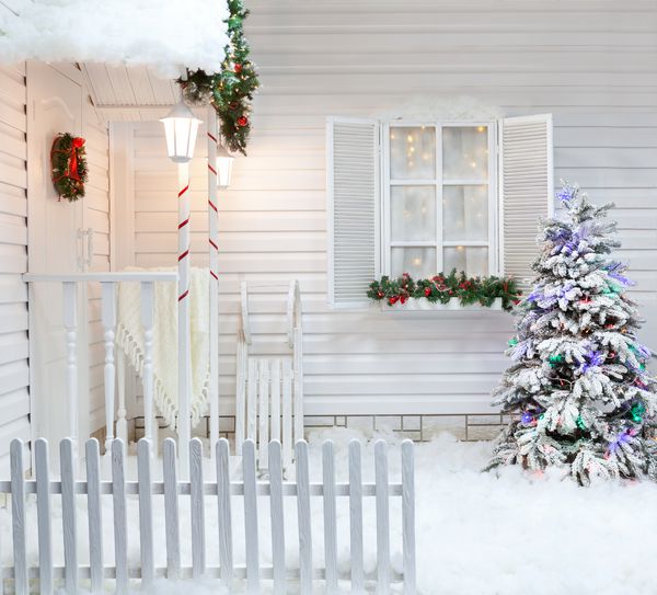 نمای بیرونی زمستانی یک خانه کشور با تزئینات کریسمس به سبک آمریکایی حیاط پوشیده از برف با ایوان درخت و سورتمه های چوبی پرنعمت