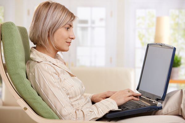 زنی که در صندلی در خانه با استفاده از رایانه لپ تاپ نشسته است در صفحه اتاق نشیمن روی صفحه کلید تایپ می کند